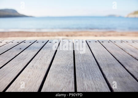 Leere Holzdeck Tabelle auf blurry Meer und Strand Hintergrund. Kopieren Sie Raum für Produkt anzeigen und zusammengesetzte Bilder. Stockfoto