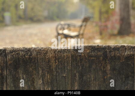 Holzzaun im Vordergrund und ein großer Garten mit Kegelbahn und Bank unscharf im Hintergrund Stockfoto