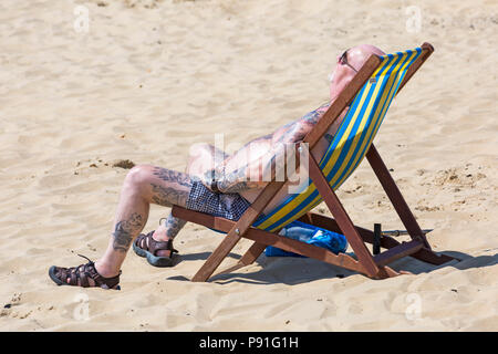 Bournemouth, Dorset, Großbritannien. 14. Juli 2018. UK Wetter: Die hitzewelle weiter mit einem anderen heißen, sonnigen Tag, als Sonnenanbeter die Wetter und Kopf an der Küste in Bournemouth Strände machen. Mann Sonnenbad im Liegestuhl. Credit: Carolyn Jenkins/Alamy leben Nachrichten Stockfoto