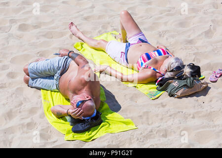 Bournemouth, Dorset, Großbritannien. 14. Juli 2018. UK Wetter: Die hitzewelle weiter mit einem anderen heißen, sonnigen Tag, als Sonnenanbeter die Wetter und Kopf an der Küste in Bournemouth Strände machen. Paar Sonnenbaden am Strand. Credit: Carolyn Jenkins/Alamy leben Nachrichten Stockfoto