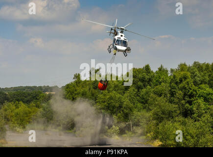 Pontypridd, Wales, 14. Juli 2018. Pontypridd, Wales, 14. Juli 2018. Kampf gegen Gras Brände mit einem Hubschrauber. Staub auf dem Boden ist, peitschte wie ein Hubschrauber aus Aufzüge mit einem Eimer Wasser. Der Hubschrauber wird verwendet, um ein Gras, das Feuer auf die graig Berghang oberhalb Pontypridd in South Wales zu kämpfen. Der Helikopter ist die Abholung von Wasser aus einem Teich auf dem Gelände der ehemaligen Cwm Koksöfen und Zeche Beddau in der Nähe von Pontypridd. Bild 14. Juli 2018. Quelle: Ceri Breeze/Alamy Leben Nachrichten genommen Stockfoto