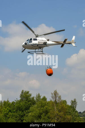 Pontypridd, Wales, 14. Juli 2018. Kampf gegen Gras Brände mit einem Hubschrauber. Ein Hubschrauber mit einem großen Eimer mit Wasser. Der Hubschrauber wird verwendet, um ein Gras, das Feuer auf die graig Berghang oberhalb Pontypridd in South Wales zu kämpfen. Es zieht Wasser aus einem Teich auf dem Gelände der ehemaligen Cwm Koksöfen und Zeche Beddau in der Nähe von Pontypridd. Bild 14. Juli 2018. Quelle: Ceri Breeze/Alamy Leben Nachrichten genommen Stockfoto