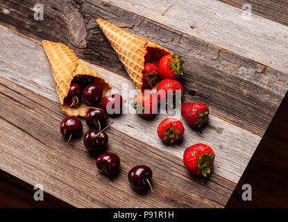 Sommer Beeren in Eistüten auf rustikalen Hintergrund. Frische Erdbeeren und Kirschen Waffeln auf hölzernen Tisch Stockfoto