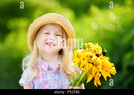 Adorable kleine Mädchen im Strohhut mit schönen gelben Blumen für Ihre Mutter auf sonnigen Sommertag Stockfoto