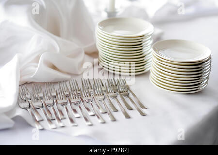 Zeile der Gabeln und Platten auf einem weißen Tischtuch. Geschirr vorbereitet für Veranstaltung gesorgt. Stockfoto