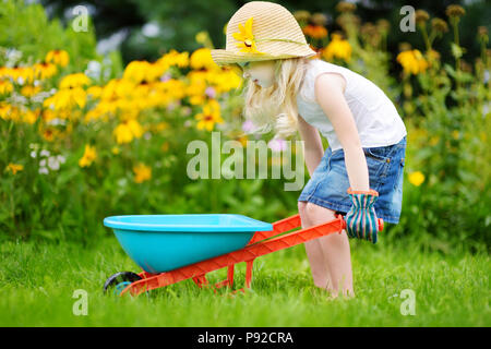 Adorable kleinen Mädchen in straw hat Spaß mit einem Spielzeug Schubkarre. Niedliche Kind spielen Farm im Freien auf Sommertag. Stockfoto