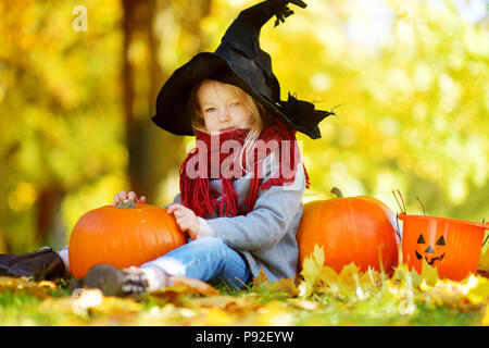 Adorable kleine Mädchen mit halloween kostüm Spaß auf einem kürbisfeld auf schönen Herbsttag. Glückliches Kind spielen im Herbst Park. Herbst activ Stockfoto