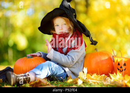 Adorable kleine Mädchen mit halloween kostüm Spaß auf einem kürbisfeld auf schönen Herbsttag. Glückliches Kind spielen im Herbst Park. Herbst activ Stockfoto