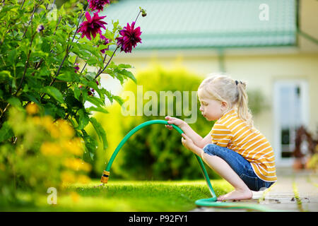 Süße kleine Mädchen Blumen gießen im Garten am Sommer, der Tag. Kind mit Gartenschlauch an einem sonnigen Tag. Mummys little Helper. Stockfoto