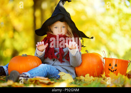 Adorable kleine Mädchen mit halloween kostüm Spaß auf einem kürbisfeld auf schönen Herbsttag. Glückliches Kind spielen im Herbst Park. Herbst activ Stockfoto