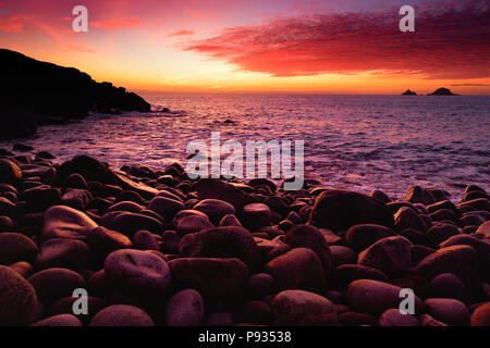 Schönen lila getönte Wellen auf einem felsigen Strand bei Sonnenuntergang über Porth Nanven im Babybett Tal von Cornwall, England brechen Stockfoto