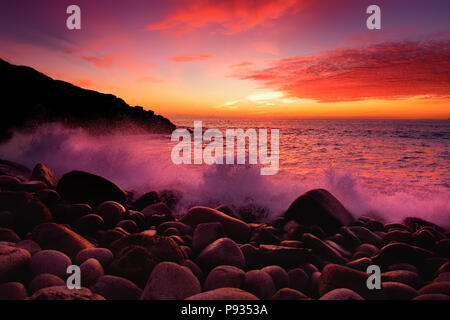 Schönen lila getönte Wellen auf einem felsigen Strand bei Sonnenuntergang über Porth Nanven im Babybett Tal von Cornwall, England brechen Stockfoto