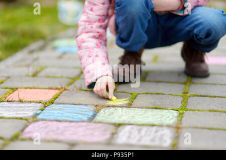 Close-up auf der Hand des kleinen Mädchens Zeichnung mit farbigen Kreiden auf einem Bürgersteig. Sommer Aktivitäten für kleine Kinder. Kreative Freizeit für Familie. Stockfoto