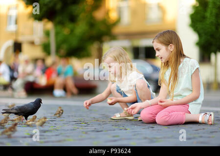 Zwei süße kleine Schwestern Fütterung Vögel auf Sommertag. Kinder füttern Tauben und Spatzen im Freien. Aktive Freizeit mit Kindern. Stockfoto