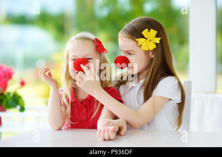 Glückliche kleine Schwestern tragen rote Nasen clown Spaß zusammen auf sonnigen Sommertag zu Hause. Zwei Kinder spielen zusammen. Stockfoto