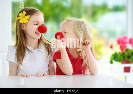 Glückliche kleine Schwestern tragen rote Nasen clown Spaß zusammen auf sonnigen Sommertag zu Hause. Zwei Kinder spielen zusammen. Stockfoto