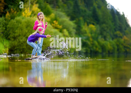 Adorable Schwestern spielen durch Hallstätter See in Österreich an einem warmen Sommertag. Süße Kinder Spaß Spritzwasser und warfen Steine in die Stockfoto