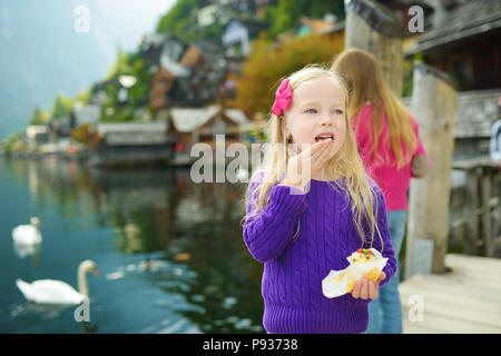 Zwei kleine Mädchen Fütterung Schwänen in Hallstatt Stadt am See in den österreichischen Alpen im schönen Abendlicht auf schönen Tag im Herbst Stockfoto