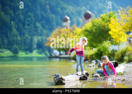 Adorable Schwestern spielen durch Konigssee See in Deutschland an einem warmen Sommertag. Süße Kinder Spaß Fütterung Enten und warfen Steine in den See. Su Stockfoto