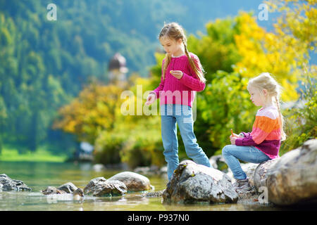 Adorable Schwestern spielen durch Konigssee See in Deutschland an einem warmen Sommertag. Süße Kinder Spaß Fütterung Enten und warfen Steine in den See. Su Stockfoto