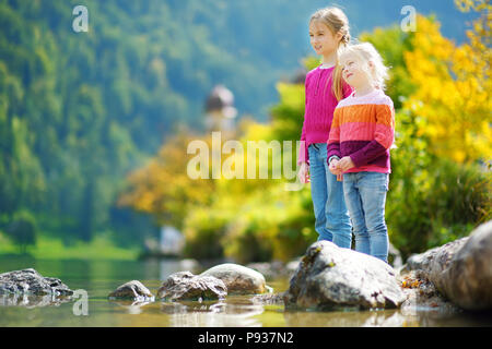 Adorable Schwestern spielen durch Konigssee See in Deutschland an einem warmen Sommertag. Süße Kinder Spaß Fütterung Enten und warfen Steine in den See. Su Stockfoto