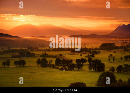 Atemberaubende morgen lansdcape der kleinen bayerischen Dorf im Nebel. Malerischer Blick auf die Bayerischen Alpen bei Sonnenaufgang mit majestätischen Bergen im Hinterg Stockfoto