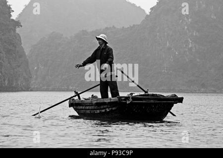 Ein Fischer bei der Arbeit an Bord eines kleinen Bootes im Wasser der Halong Bay - VIETNAM Stockfoto