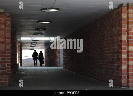 Zwei Personen Silhouette gegen ein helles Licht zu Fuß durch einen Tunnel mit gemauerten Wänden auf die Kamera Stockfoto