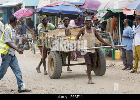 Kakuma, Kenia - Tageloehner ziehen eine große Transportanhänger mit Waren beladen auf einem belebten, über einen unbefestigten Weg. Stockfoto