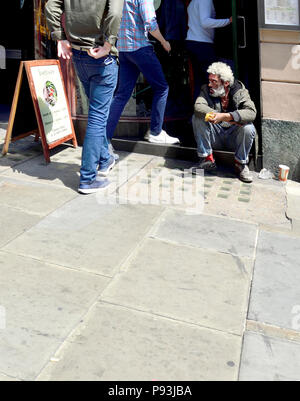 Schwarzer Mann mit weissem Haar und Bart sitzen auf den Schritt in ein Restaurant wie die Menschen in ihm vorbei gehen, Whitehall, London, England, UK. Stockfoto