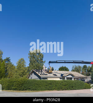 Großen Kran Bereitstellung neuer Dachziegel zu Dachdecker, Arbeiter oder Handwerker arbeiten an einem freistehenden Bungalow Haus Stockfoto