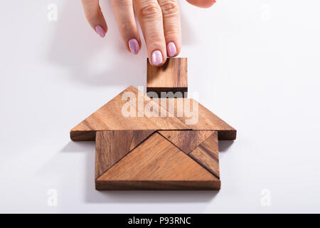 Ansicht von der Frau Hand Gebäude Haus mit Holz Tangram Puzzle auf weißem Hintergrund Stockfoto