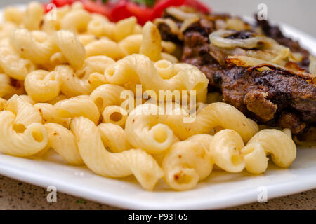 Gekocht auf hausgemachte Nudeln mit gebratenem Schweinefleisch oder Rindfleisch, und weiße Soße, liegen auf einem weißen Teller. Das Konzept der hausgemachten appetitliches Essen. Selektive konzentrieren. Stockfoto