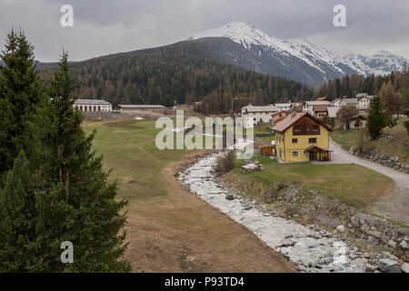 Blick über ein kleines Dorf in der Nähe des Flusses Vallember in der Schweiz mit schneebedeckten Bergen im Hintergrund, Bild von Süden Zernez Schweiz. Stockfoto