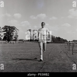 1967, historicall, erwachsenen männlichen Athleten mit einfachen T-Shirt und Shorts Training im Freien auf einer Grasbahn, England, UK. Stockfoto