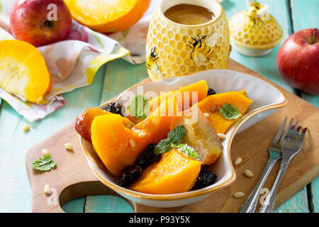 Kürbis gebacken mit Äpfel, Pflaumen und Gewürzen in eine Schüssel auf einen hölzernen Tisch. Diätmenü. Das Konzept der gesunden Ernährung. Stockfoto