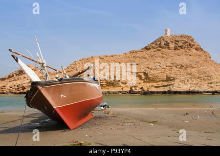 OMAN, Ash Sharqiyah Region, Sur, Boote am Strand mit Turm von Al Ayajh Fort an der Rückseite Stockfoto