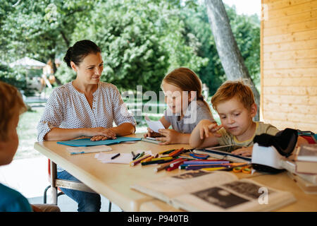 Junge Mädchen vorlesen zu ihrer Mutter und Klassenkameraden. Homeschooling - Kinder lernen mit einem Lehrer in einem Park. Stockfoto