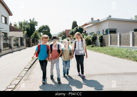 Primäre Kinder zu Fuß auf der Straße auf ihren ersten Schultag. Eine Gruppe von Happy Mitschüler zu Fuß auf ihren eigenen Spaß an der Schule. Stockfoto