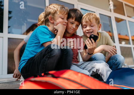 Kinder mit einem Handy eine selfie außerhalb der Schule. Gruppe von elementaren Studenten Spaß spielen mit einem Handy. Stockfoto