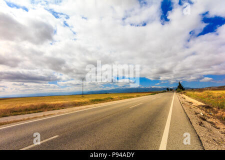 Landschaft der Straße durch goldene Felder mit Wolken, Provinz Granada, Spanien Stockfoto