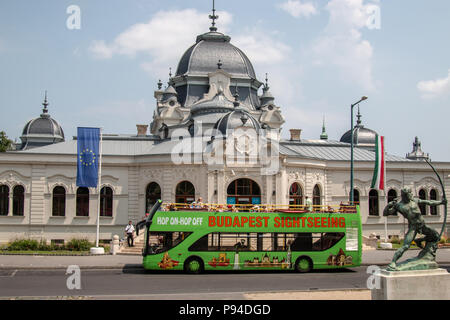 Eine grüne Tour Bus sitzt vor einem wunderschönen Gebäude in der Nähe der Helden Platz, Budapest, Ungarn. Stockfoto