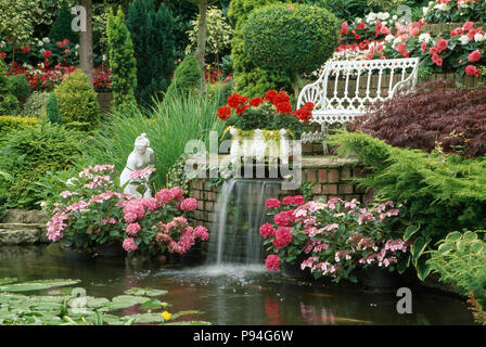 Wasser im Garten mit Teich und Wasserfall. Weiß mit rosa Hortensien, begoniasand Geranien. Stockfoto