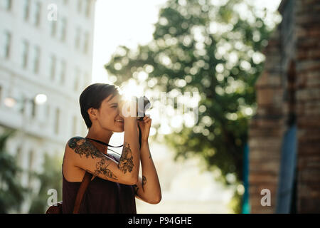 Frau Reisenden, Fotos mit Ihrer Kamera mit Sonne in den Hintergrund. Tourist mit Tattoo auf der Hand gehen in der Stadt fotografieren. Stockfoto