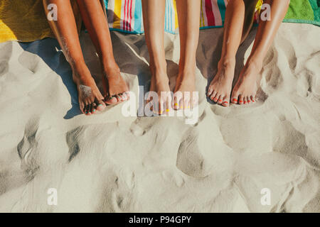 Nahaufnahme der Beine von drei Frauen sitzen am Strand mit Nägeln in verschiedenen Farben lackiert. Stockfoto