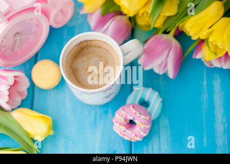 Frühling Morgen, duftenden Kaffee und Tulpen gelb und rosa Farbe. Donuttsy Kopien. Blau Holz- Hintergrund, Platz für Text und Postkarte. Stockfoto