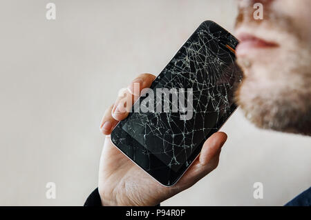 Der Kerl ist ein Gespräch mit einem defekten Bildschirm. BlackBerry-Smartphone mit zersprungenem Glas in der Hand eines Mannes. Kopieren Sie Raum. Copyspace. Stockfoto