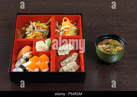 Bento Box mit Sushi und Brötchen, Miso Suppe auf einem Holztisch. Stockfoto