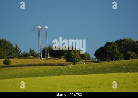 Paar von Windenergieanlagen auf einem Schottischen Bauernhof von pulsierenden grünen Weide und Nadelbaum Plantage. Juli, 2018. Stockfoto