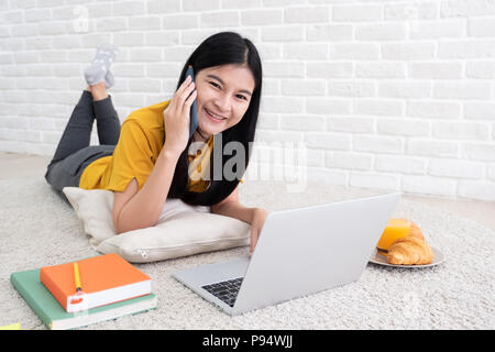 Asiatische Frau Vortrag über Handy und Laptop zu Hause zu arbeiten. Frau auf dem Teppich an der Wand legen. online arbeiten Lifestyle Stockfoto